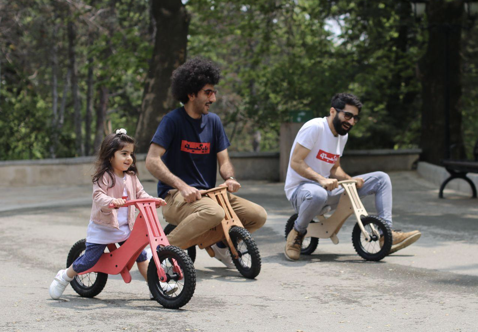 A child and two adults riding Bikkido balance bicycles in a park