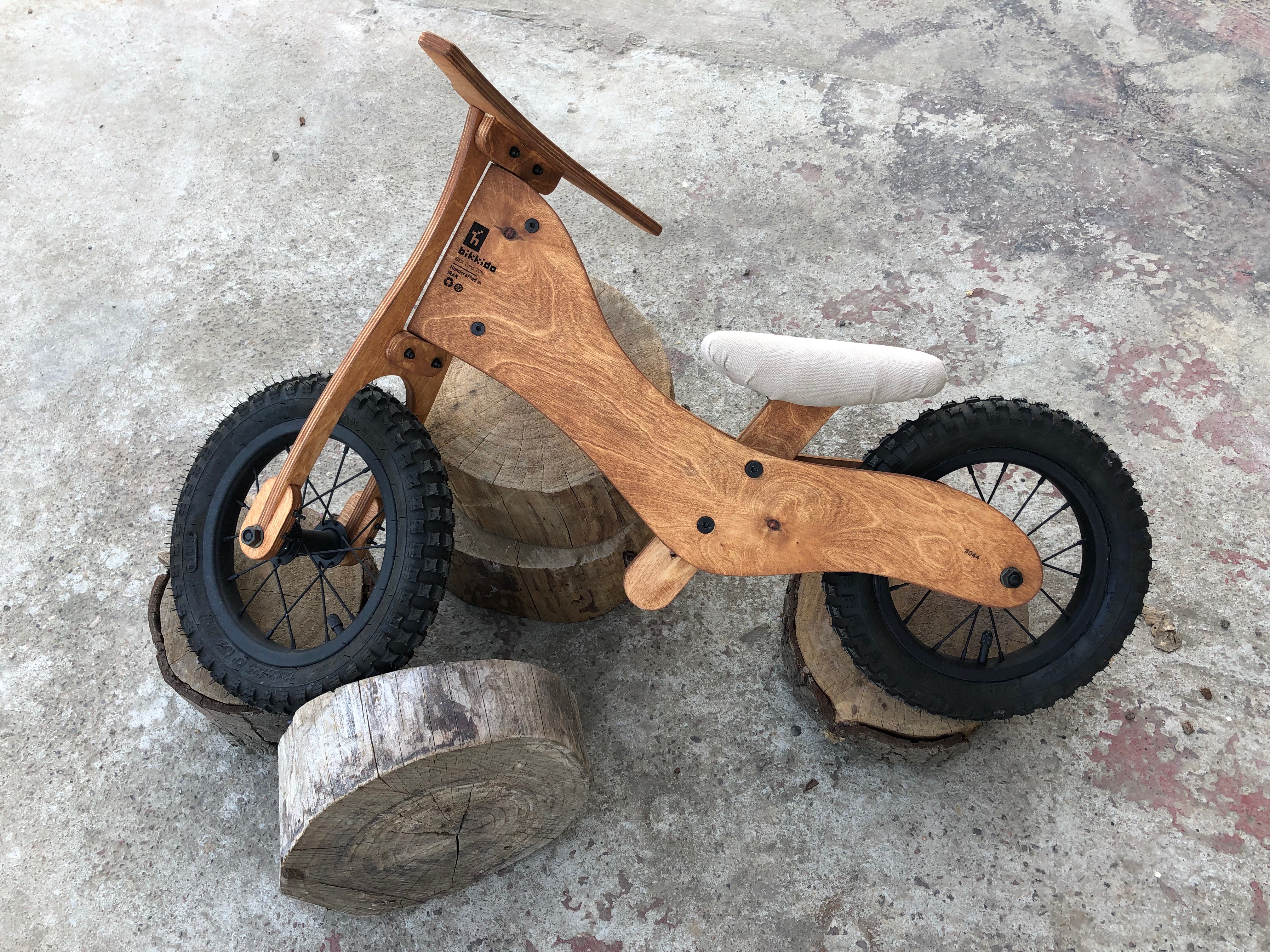 A wooden balance bicycle resting on the ground